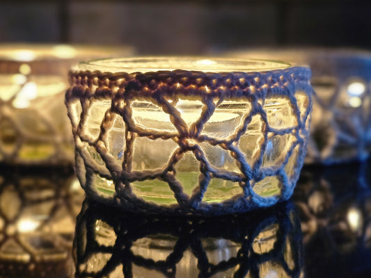 Glass candle holders with crochet covers on a reflective surface.
