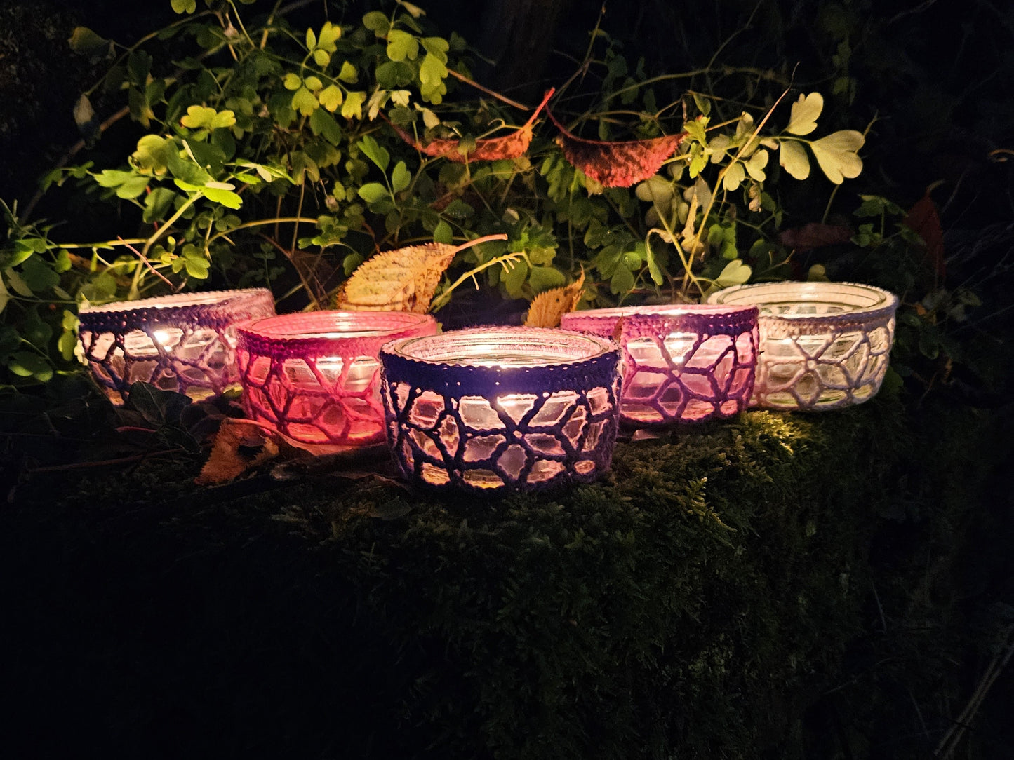 Decorative glass lanterns glowing in the dark with plants around