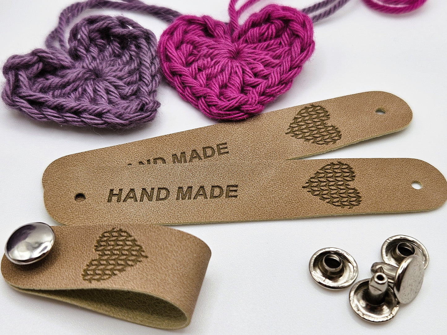Beige faux leather tag with a snap-on popper, engraved with the word "HAND MADE" and a heart design.