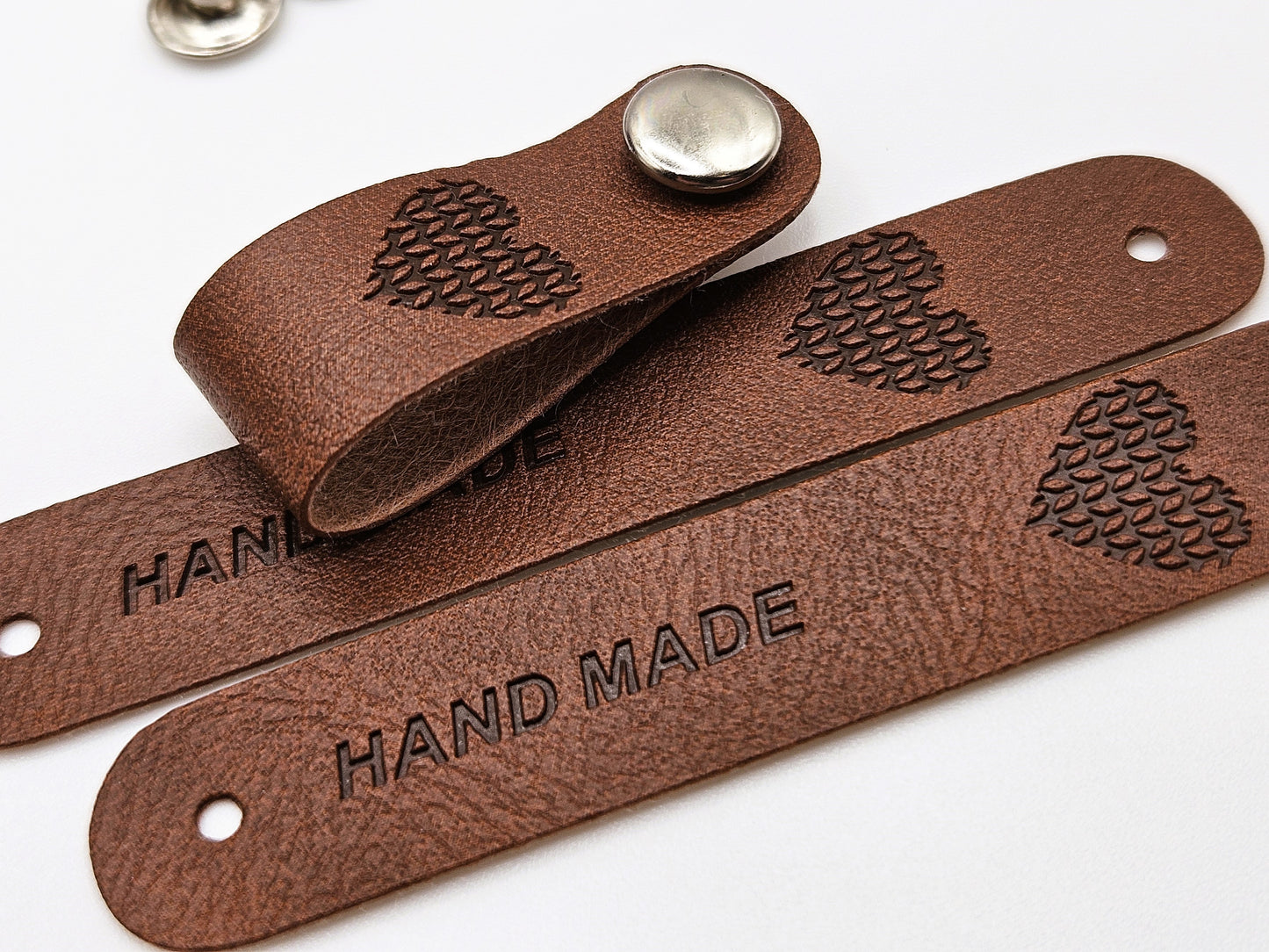 Brown faux leather hand made tag with a snap-on popper, engraved with the word "HAND MADE" and a heart design.