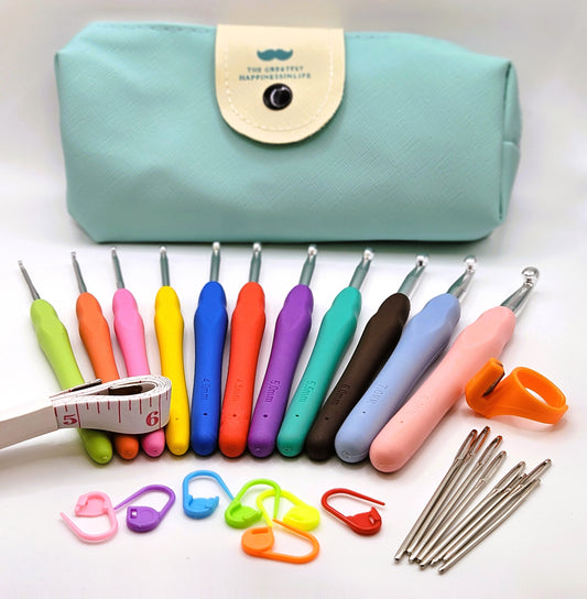 Complete beginner's crochet hook starter kit including soft grip ergonomic hooks, darning needles, stitch markers, thread cutter, and a measuring tape, laid out in front of a mint green storage case.