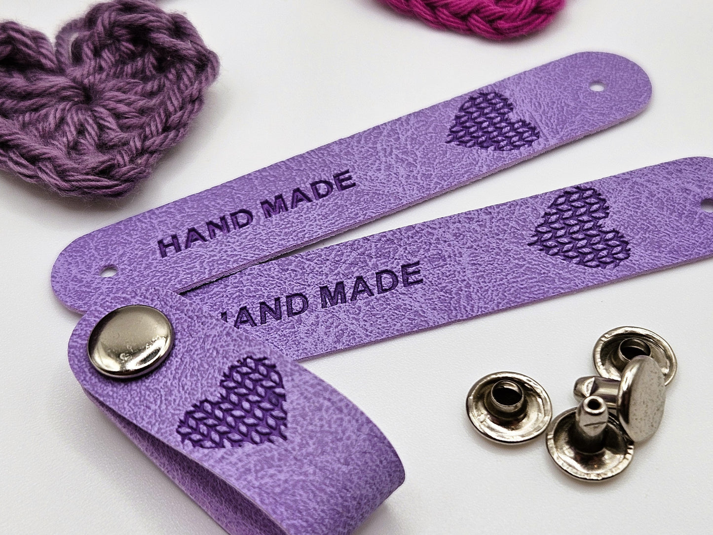 Purple faux leather hand made tag with a snap-on popper, engraved with the word "HAND MADE" and a heart design.