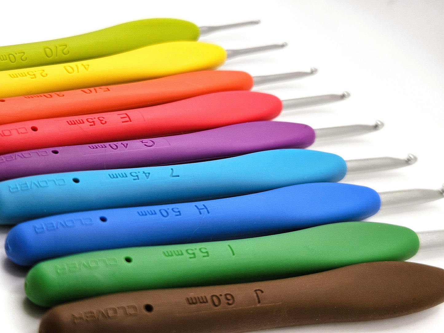 Set of Clover Amour Crochet Hooks arranged in a gradient of vibrant colours, with size markings clearly visible on their handles and metal tips pointing outward.