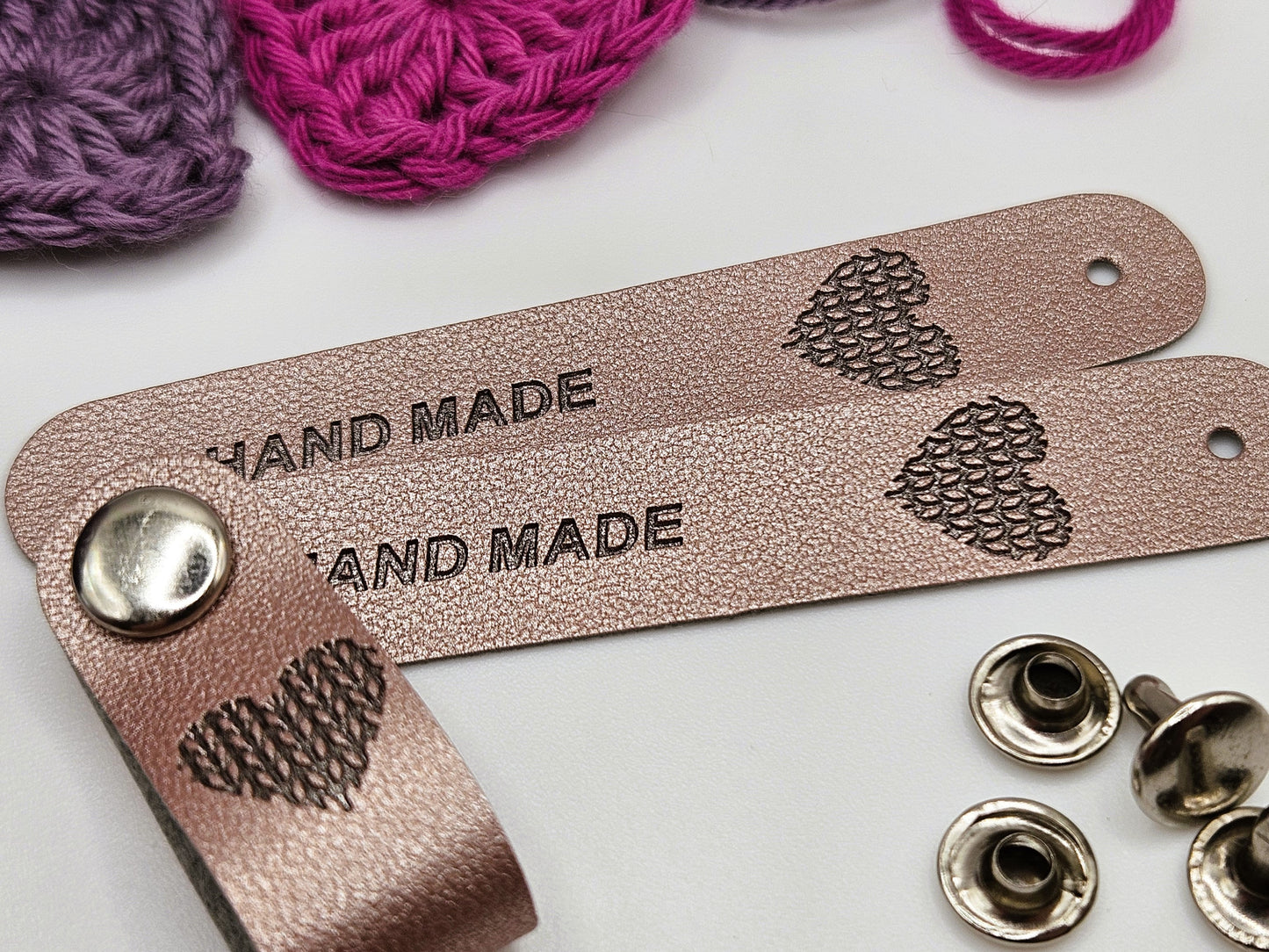 Silver faux leather hand made tag with a snap-on popper, engraved with the word "HAND MADE" and a heart design.