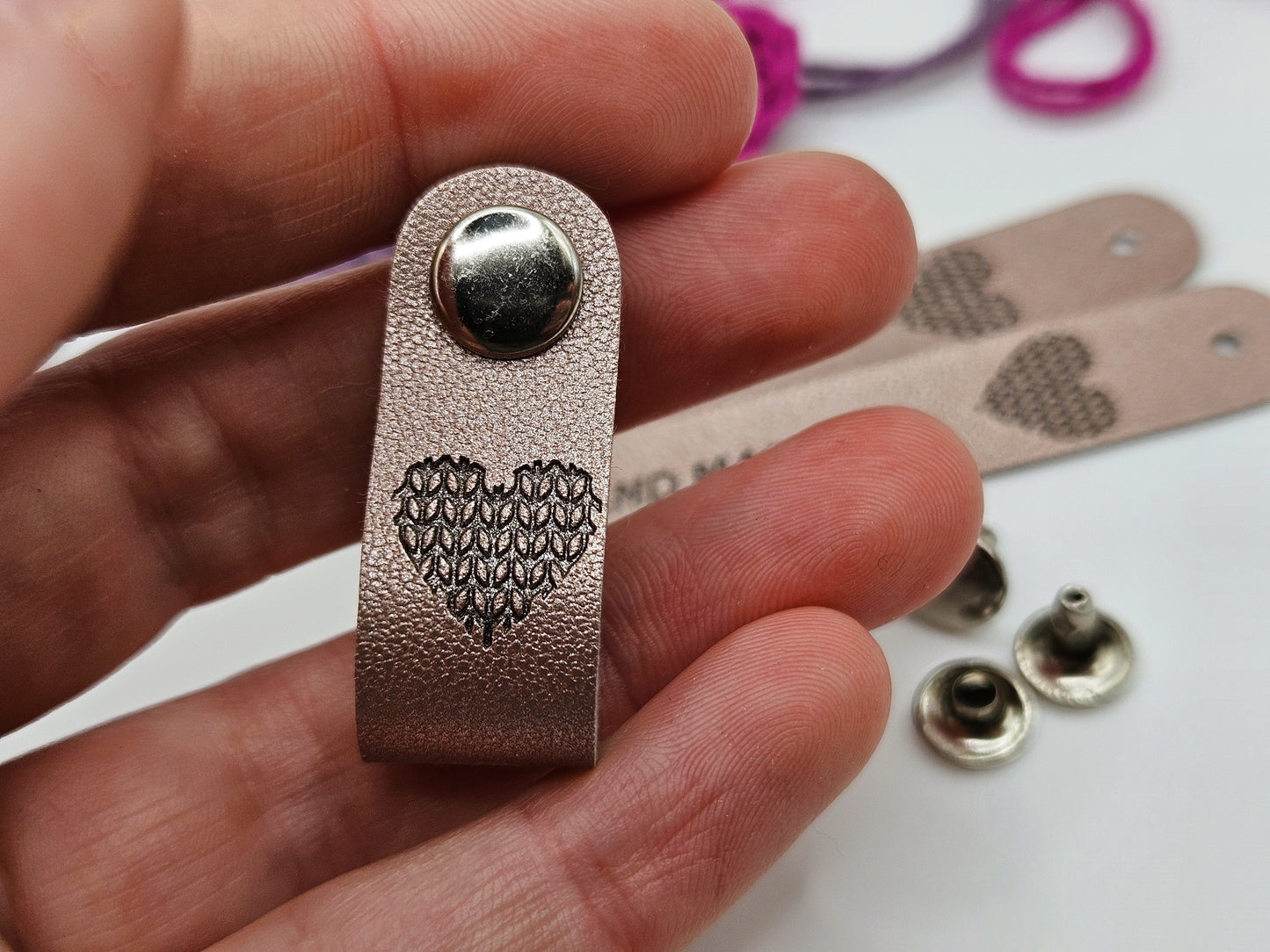 Silver faux leather hand made tag with a snap-on popper, held in a hand with a heart design showing.