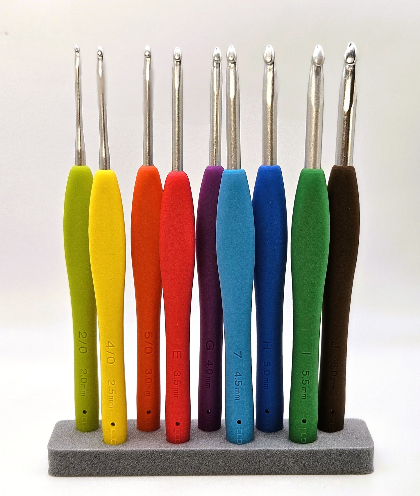 Clover Amour Crochet Hooks displayed upright in a foam holder, showing their vibrant handles and polished metal tips, with size markings clearly visible.
